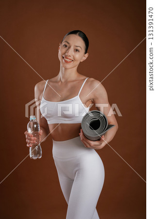 Fresh water in bottle and yoga mat. Beautiful fitness woman is in the studio Fresh water in bottle and yoga mat. Beautiful fitness woman is in the studio 131391470