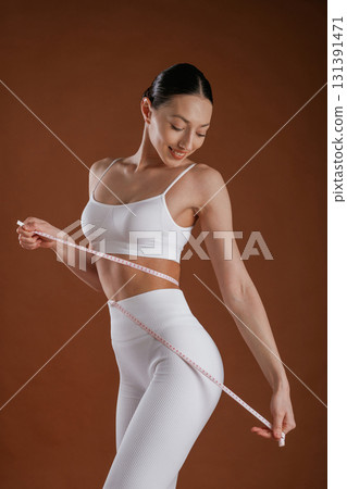 Measuring tape on the waist. Beautiful fitness woman is in the studio Measuring tape on the waist. Beautiful fitness woman is in the studio 131391471