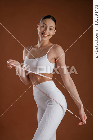 Measuring tape on the waist. Beautiful fitness woman is in the studio Measuring tape on the waist. Beautiful fitness woman is in the studio 131391473