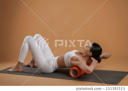 Using roll on the yoga mat. Beautiful fitness woman is in the studio 131391513