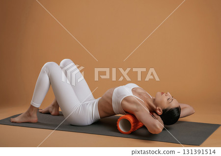 Using roll on the yoga mat. Beautiful fitness woman is in the studio Using roll on the yoga mat. Beautiful fitness woman is in the studio 131391514