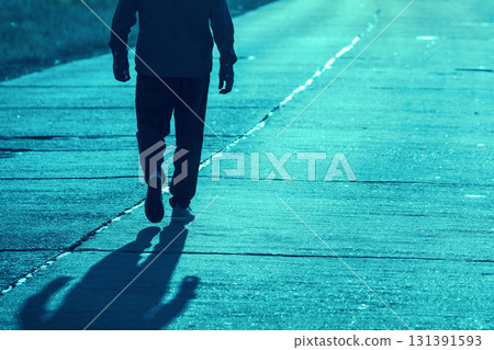 A human walks in the street on a concrete road in the evening at sunset light. Blue toning A human walks in the street on a concrete road in the evening at sunset light. Blue toning 131391593