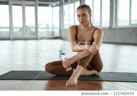 Sitting with bottle of water, break. Fitness woman in sportswear is indoors 131392039