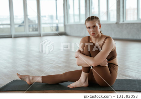 Sitting on yoga mat, taking a break. Fitness woman in sportswear is indoors Sitting on yoga mat, taking a break. Fitness woman in sportswear is indoors 131392058