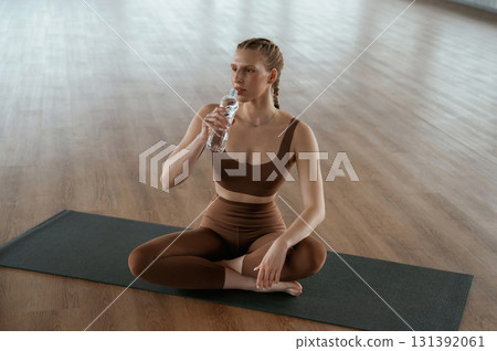 Taking a break, with bottle of water. Fitness woman in sportswear is indoors Taking a break, with bottle of water. Fitness woman in sportswear is indoors 131392061