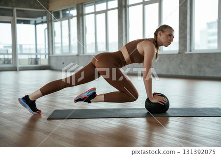 Using fitness ball on yoga mat. Woman in sportswear is indoors Using fitness ball on yoga mat. Woman in sportswear is indoors 131392075