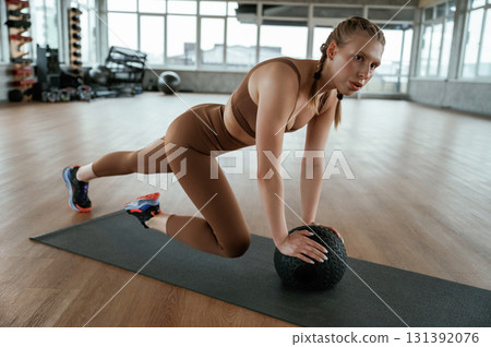 Using fitness ball on yoga mat. Woman in sportswear is indoors 131392076