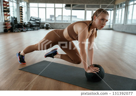 Using fitness ball on yoga mat. Woman in sportswear is indoors Using fitness ball on yoga mat. Woman in sportswear is indoors 131392077