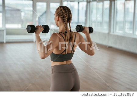 With dumbbells in hands. Fitness woman in sportswear is indoors 131392097