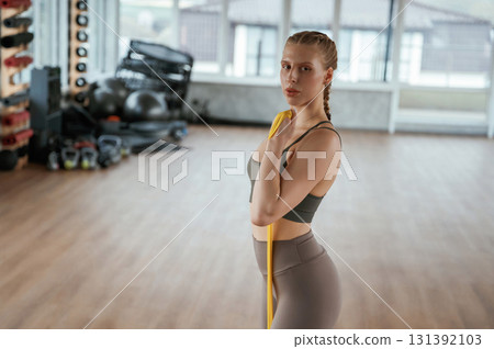 Yellow strap for stretching. Fitness woman in sportswear is indoors 131392103