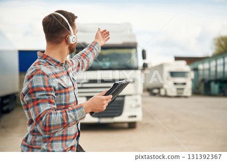Showing the way, with tablet. Man is standing against trucks outdoors Showing the way, with tablet. Man is standing against trucks outdoors 131392367