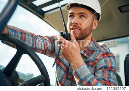 Walkie talkie device, conversation, orders. Man is with tractor. Agricultural worker Walkie talkie device, conversation, orders. Man is with tractor. Agricultural worker 131392397