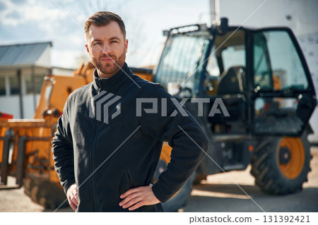 In black hoodie. Standing and posing. Man is with tractor. Agricultural worker In black hoodie. Standing and posing. Man is with tractor. Agricultural worker 131392421
