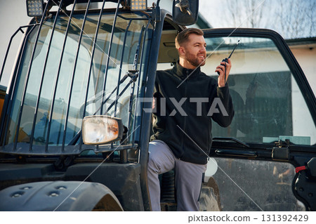 Communication with other people by walkie talkie. Man is with tractor. Agricultural worker 131392429