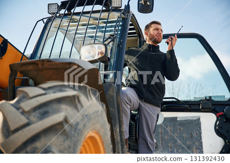 View from below, using walkie talkie. Man is with tractor. Agricultural worker 131392430