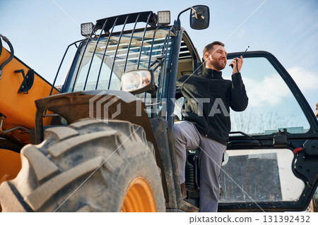 View from below, using walkie talkie. Man is with tractor. Agricultural worker View from below, using walkie talkie. Man is with tractor. Agricultural worker 131392432