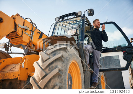 View from below, using walkie talkie. Man is with tractor. Agricultural worker View from below, using walkie talkie. Man is with tractor. Agricultural worker 131392433