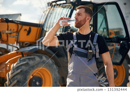 Drinking water, taking a break, tired. Man is with tractor. Agricultural worker Drinking water, taking a break, tired. Man is with tractor. Agricultural worker 131392444