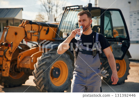 Drinking water, taking a break, tired. Man is with tractor. Agricultural worker Drinking water, taking a break, tired. Man is with tractor. Agricultural worker 131392446