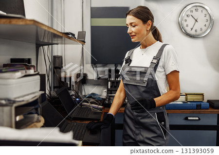 A Female Technician is Actively Working in a Workshop with Her Laptop to Enhance Productivity A Female Technician is Actively Working in a Workshop with Her Laptop to Enhance Productivity 131393059
