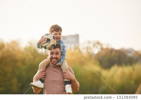 On shoulders, with soccer ball. Happy father with son are having fun on the field at summertime 131393095