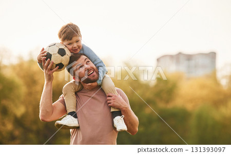 On shoulders, with soccer ball. Happy father with son are having fun on the field at summertime On shoulders, with soccer ball. Happy father with son are having fun on the field at summertime 131393097