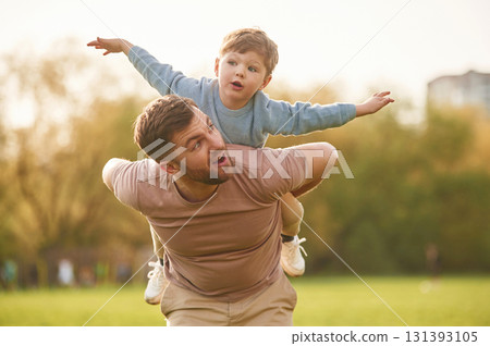 Sitting on man's shoulders. Happy father with son are having fun on the field at summertime 131393105