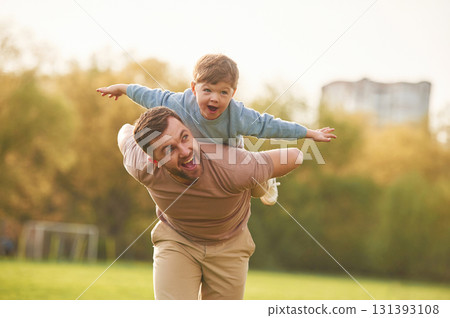 Wellbeing, kid is on the shoulders or back. Happy father with son are having fun on the field at summertime Wellbeing, kid is on the shoulders or back. Happy father with son are having fun on the field at summertime 131393108