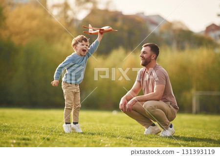 Weekend activities. Playing with toy plane. Happy father with son are having fun on the field at summertime Weekend activities. Playing with toy plane. Happy father with son are having fun on the field at summertime 131393119