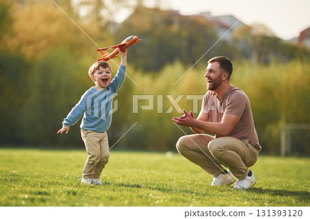 Weekend activities. Playing with toy plane. Happy father with son are having fun on the field at summertime Weekend activities. Playing with toy plane. Happy father with son are having fun on the field at summertime 131393120
