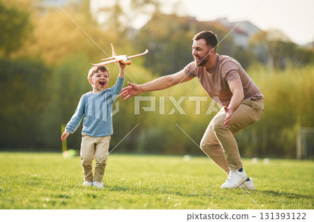 In casual clothes. Running with toy plane. Happy father with son are having fun on the field at summertime In casual clothes. Running with toy plane. Happy father with son are having fun on the field at summertime 131393122