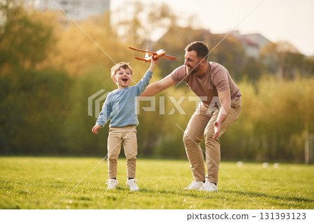 In casual clothes. Running with toy plane. Happy father with son are having fun on the field at summertime In casual clothes. Running with toy plane. Happy father with son are having fun on the field at summertime 131393123