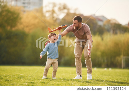 In casual clothes. Running with toy plane. Happy father with son are having fun on the field at summertime In casual clothes. Running with toy plane. Happy father with son are having fun on the field at summertime 131393124