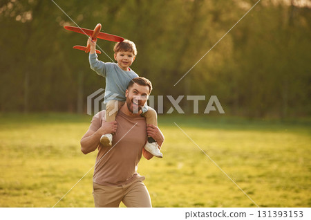 Flying high, holding toy plane, running. Happy father with son are having fun on the field at summertime Flying high, holding toy plane, running. Happy father with son are having fun on the field at summertime 131393153
