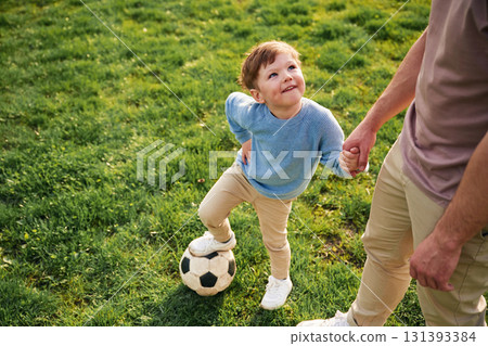 Game of soccer. With ball. Happy father with son are having fun on the field at summertime Game of soccer. With ball. Happy father with son are having fun on the field at summertime 131393384