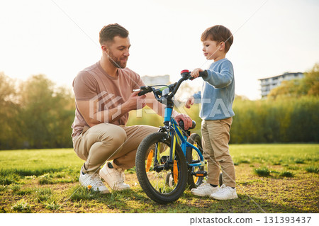 Trying the bicycle. Happy father with son are having fun on the field at summertime Trying the bicycle. Happy father with son are having fun on the field at summertime 131393437
