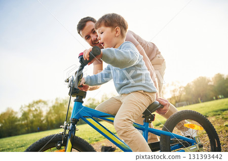 Riding on the blue bicycle. Happy father with son are having fun on the field at summertime Riding on the blue bicycle. Happy father with son are having fun on the field at summertime 131393442