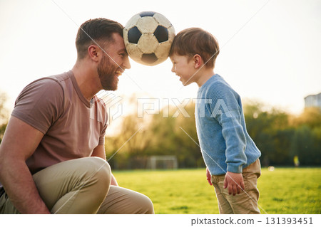 Soccer ball, holding it by heads, fun. Happy father with son are on the field at summertime 131393451