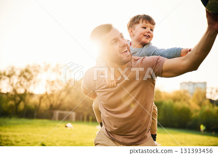 On shoulders, with soccer ball. Happy father with son are having fun on the field at summertime On shoulders, with soccer ball. Happy father with son are having fun on the field at summertime 131393456