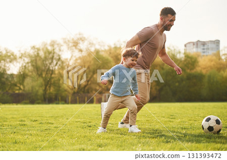 Teaching how to play a soccer. Happy father with son are having fun on the field at summertime 131393472