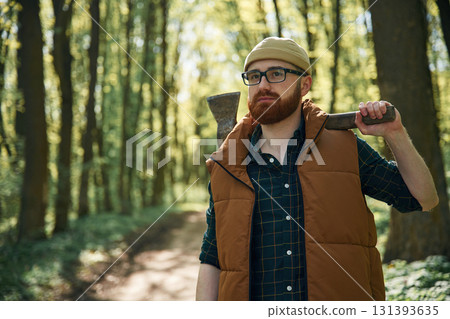 Holding an axe. Bearded man is in the forest at daytime 131393635