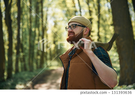Holding an axe. Bearded man is in the forest at daytime 131393636