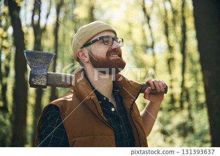 Holding an axe. Bearded man is in the forest at daytime 131393637