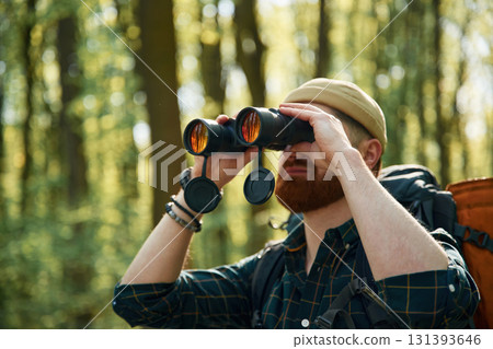 Tourist with binoculars. Bearded man is in the forest at daytime 131393646