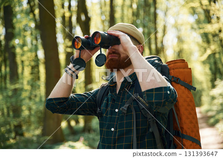 Using binoculars. Bearded man is in the forest at daytime Using binoculars. Bearded man is in the forest at daytime 131393647