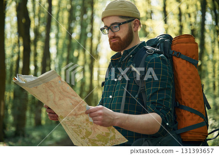 Reading the map, looking for a way. Bearded man is in the forest at daytime Reading the map, looking for a way. Bearded man is in the forest at daytime 131393657