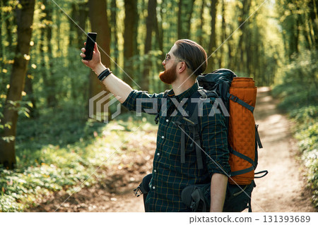 Phone in hand. Bearded man is in the forest at daytime Phone in hand. Bearded man is in the forest at daytime 131393689