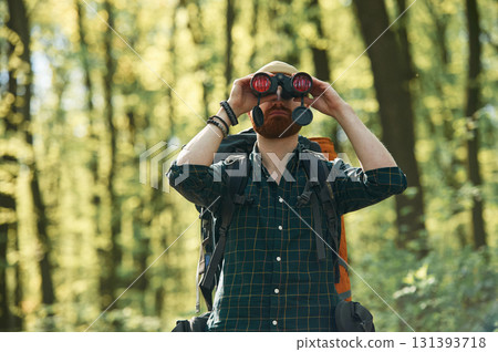 Discovering new place with binoculars. Bearded man is in the forest at daytime Discovering new place with binoculars. Bearded man is in the forest at daytime 131393718