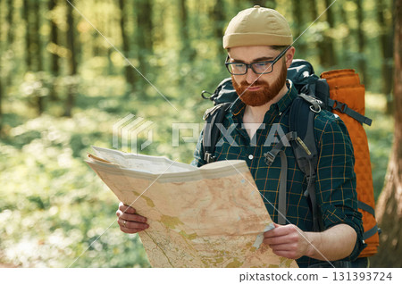 Focused on reading the map. Bearded man is in the forest at daytime Focused on reading the map. Bearded man is in the forest at daytime 131393724