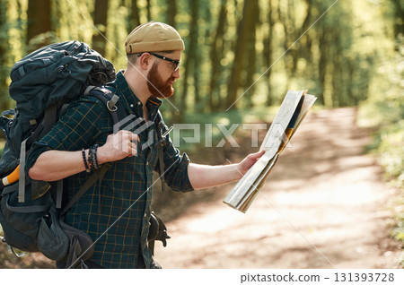 Focused on reading the map. Bearded man is in the forest at daytime 131393728